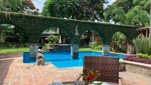 A poolside area with a stone pathway, a dining table with a vase of flowers, and a view of a pool under a green archway. - Hotel Boutique La Joyita (Cuernavaca)
