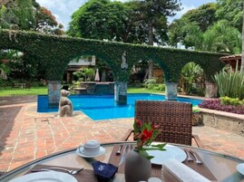 Zona de piscina con un camino de piedra, una mesa de comedor con un florero y vistas a una piscina bajo un arco verde.