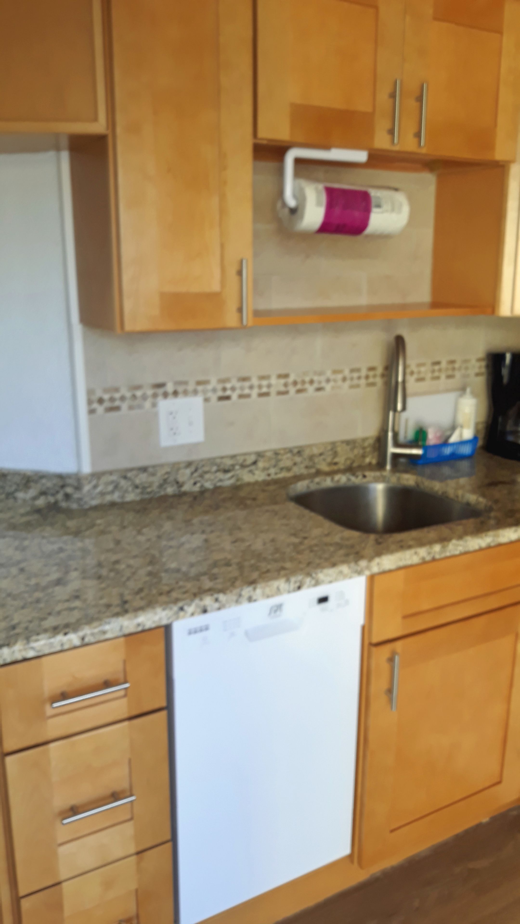 A kitchen with wooden cabinets, a granite countertop, a stainless steel sink, and a white dishwasher.