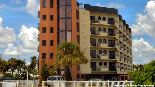 A multi-story hotel with balconies, a palm tree in front, and a clear sky.