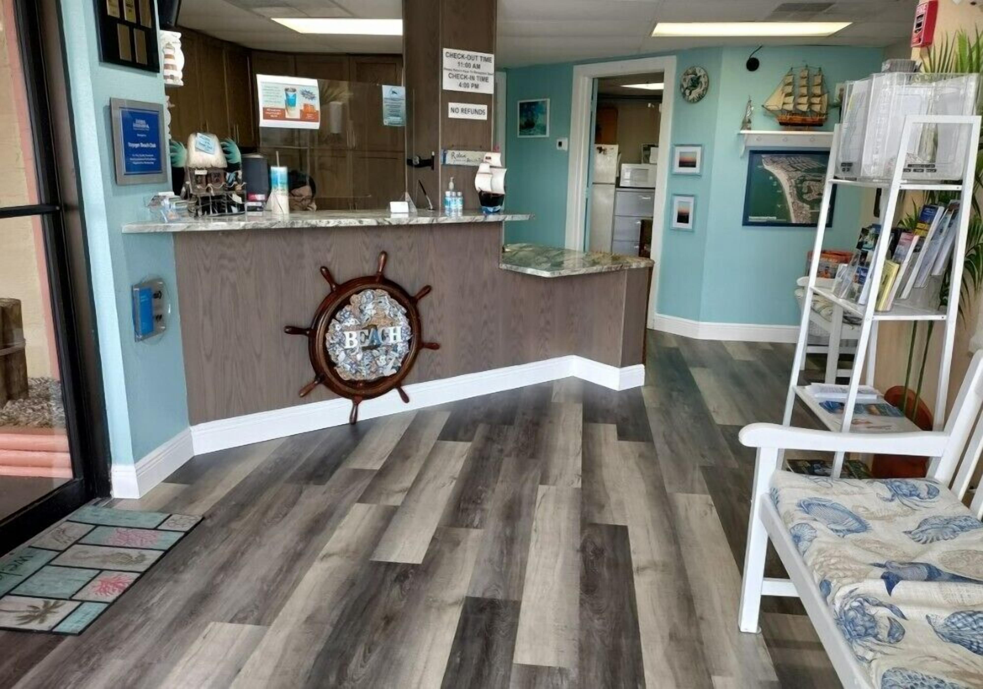 A reception area with a wooden counter, a ship's wheel, and a check-out time sign.