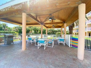 A covered outdoor seating area with hexagonal tile flooring, white metal railings, and blue and white chairs. - Sunrise Resort by Liberté (St. Pete Beach)