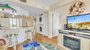 A compact living space with a kitchen, dining area, and a TV displaying a coastal view.