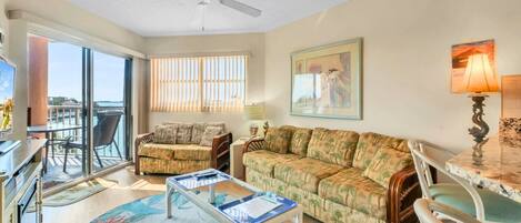 A living room with a sofa, chairs, a coffee table, and a balcony with a view of the ocean.
