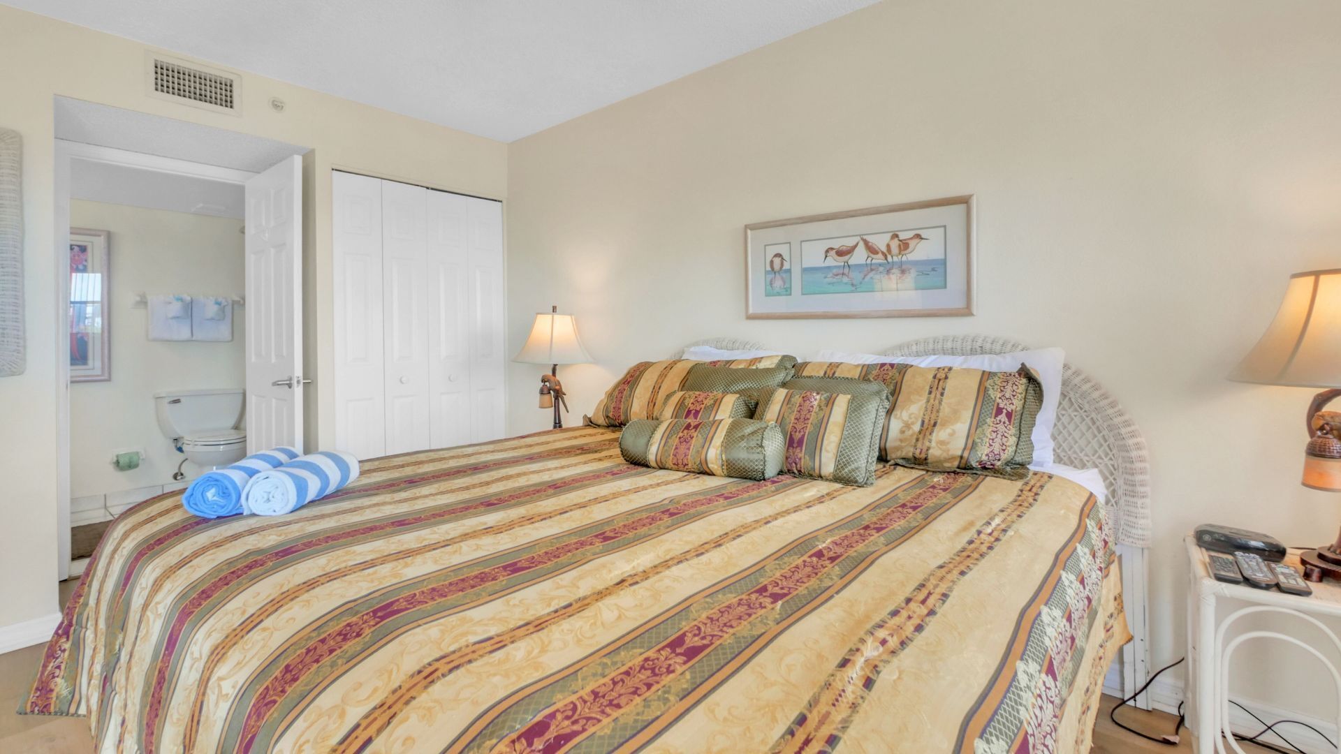 A bedroom with a large bed, a bedside table with a lamp, a framed picture on the wall, and a door leading to a bathroom.