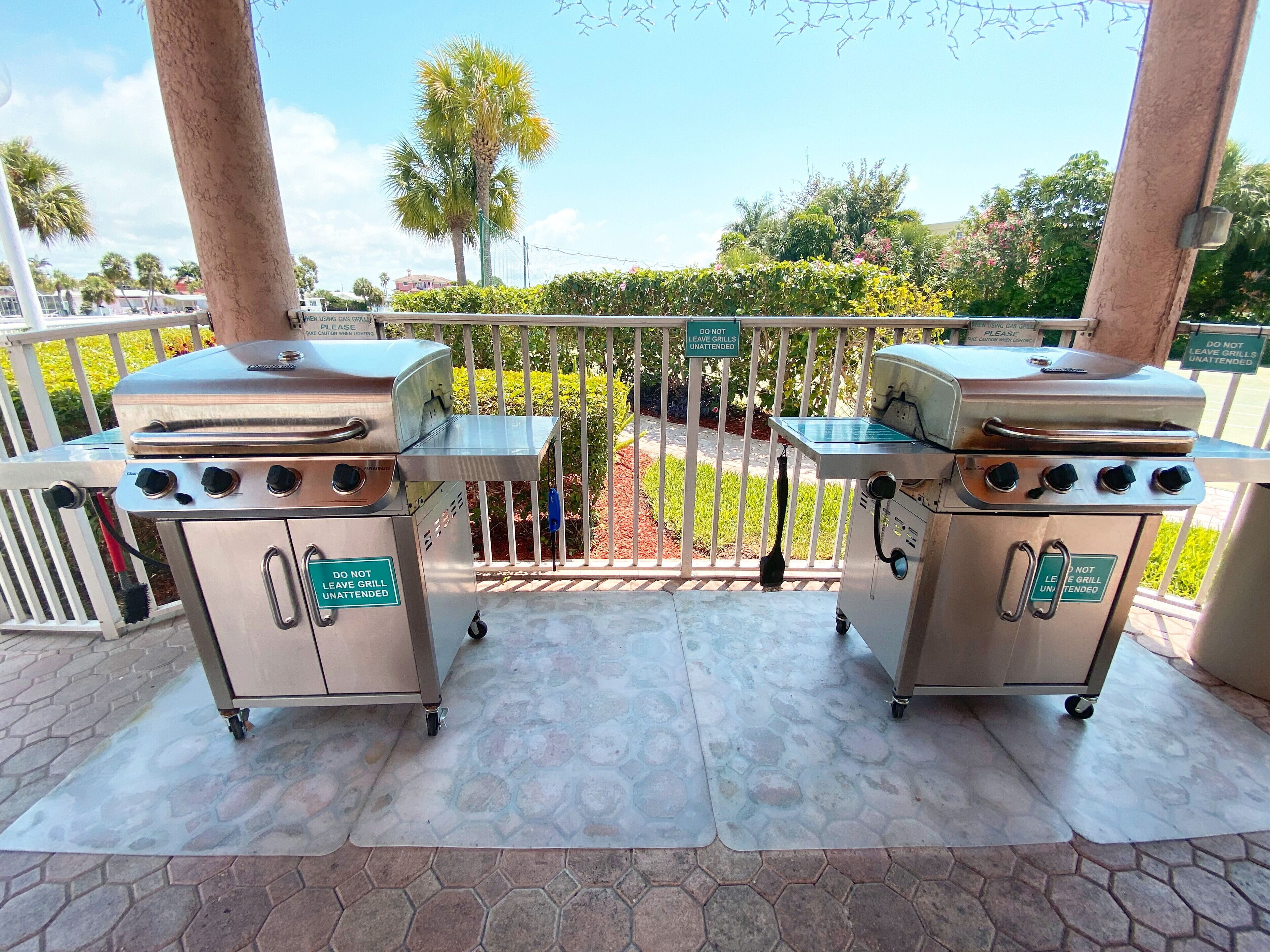 Deux barbecues à gaz portables sur une terrasse, avec un panneau indiquant : « Ne laissez pas les barbecues sans surveillance. »