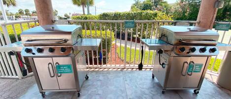 Dos parrillas de gas portátiles en un patio con un letrero que dice 'No deje las parrillas desatendidas'.