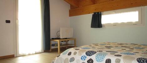 A bedroom with a bed, a desk, a computer, and a window.