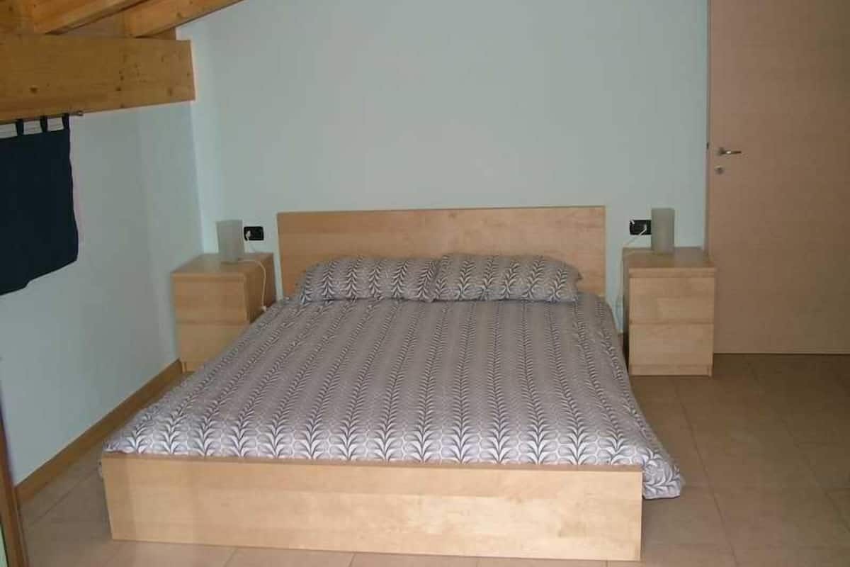 A bedroom with a wooden bed frame, a patterned bedspread, two bedside tables, and a door.