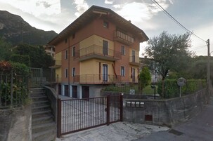 Un edificio de varios pisos con balcones, una entrada protegida por una reja y montañas al fondo.