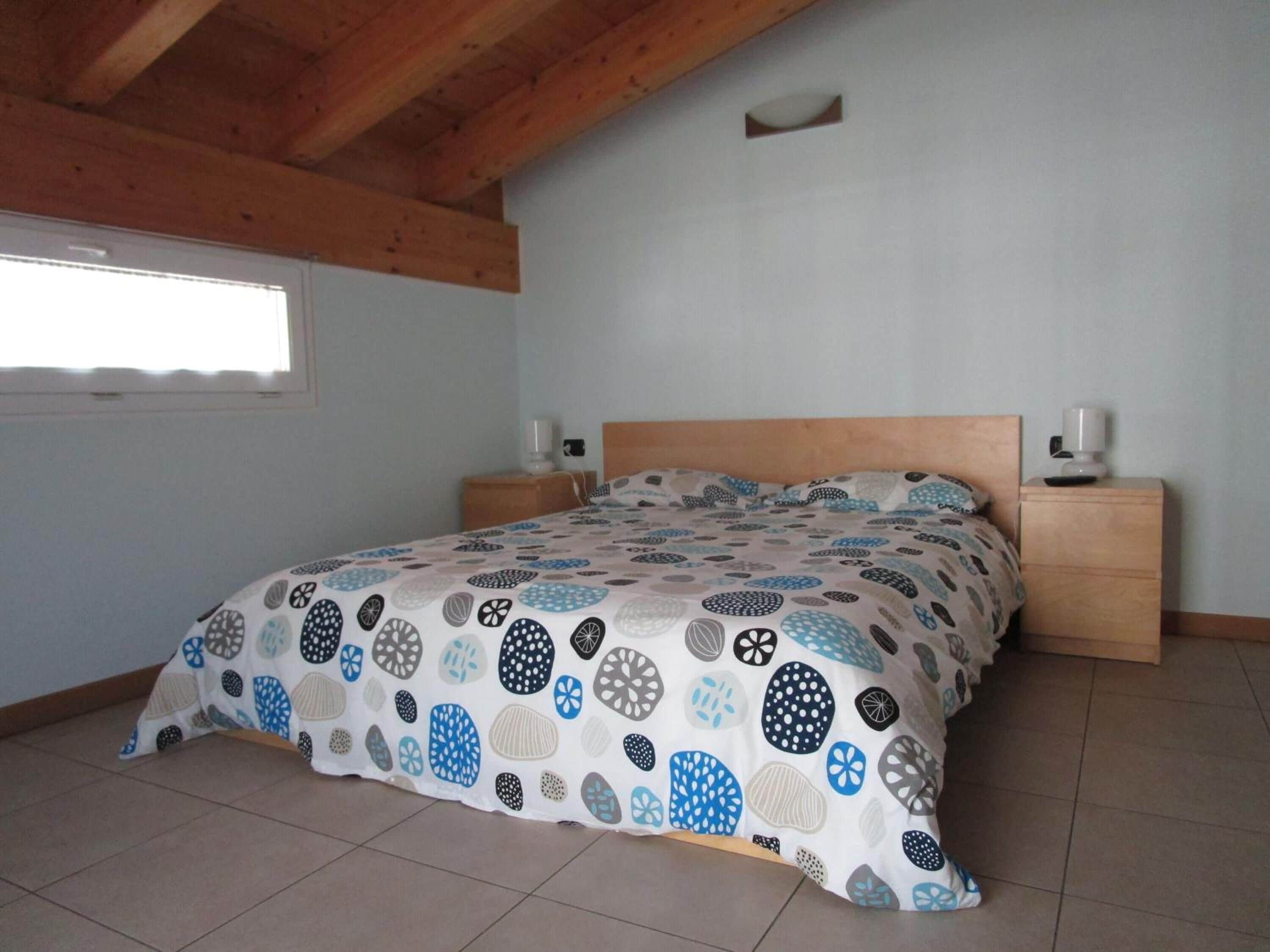 Een slaapkamer met een bed, een houten hoofdbord, twee nachtkastjes en een raam.