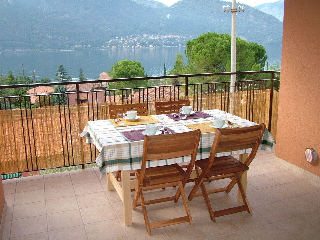 A balcony with a table set for two, overlooking a lake and mountains.
