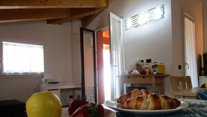 Une table de petit-déjeuner avec une assiette de croissants et des fraises, un fruit jaune, et une machine à café en arrière-plan.