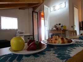 Una mesa de desayuno con un plato de croissants y fresas, una fruta amarilla y una máquina de café al fondo.
