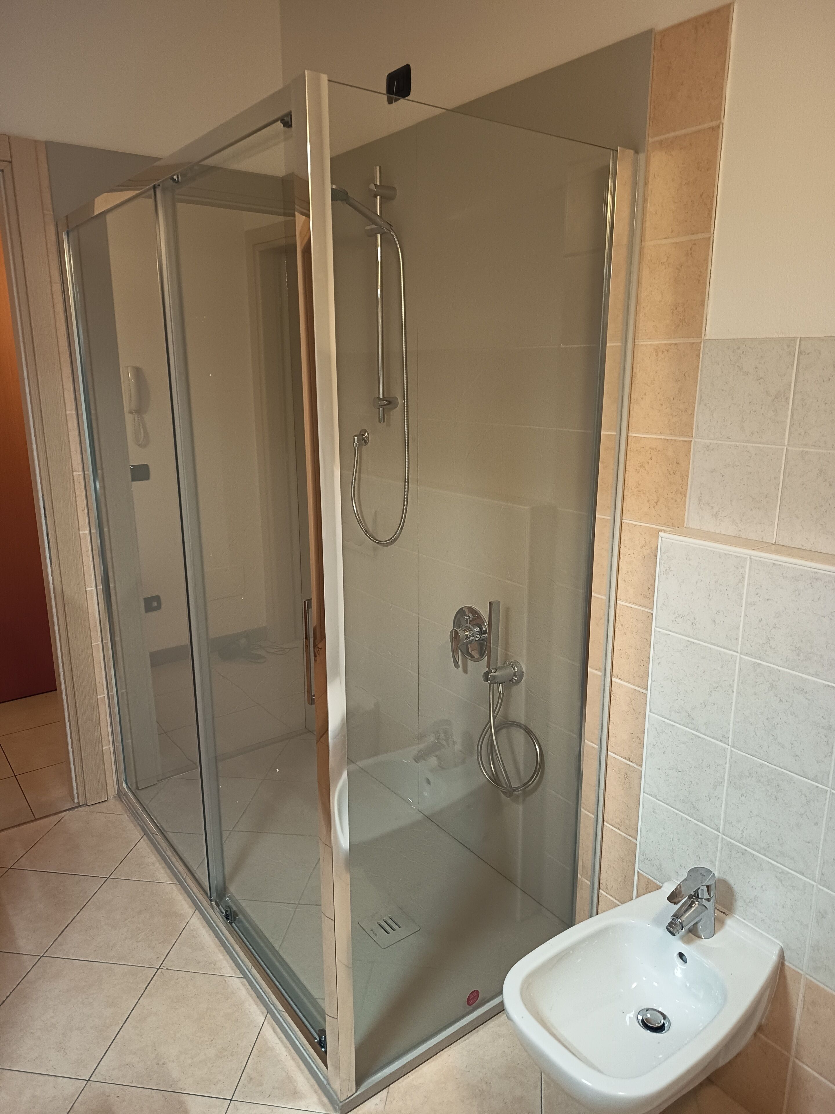 A glass-enclosed shower with a handheld showerhead and a wall-mounted faucet.