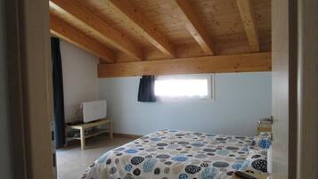 A bedroom with a wooden ceiling, a bed with a patterned bedspread, a small window, and a bedside table.