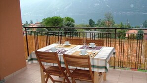 Un balcon avec une table dressée pour deux personnes, des chaises et une vue sur un lac et des montagnes.