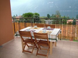 Un balcón con una mesa para dos, sillas y vistas a un lago y montañas.