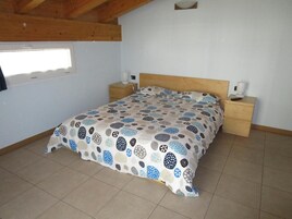 Un dormitorio con una cama, dos mesitas de noche, un ventanal y techo de madera.