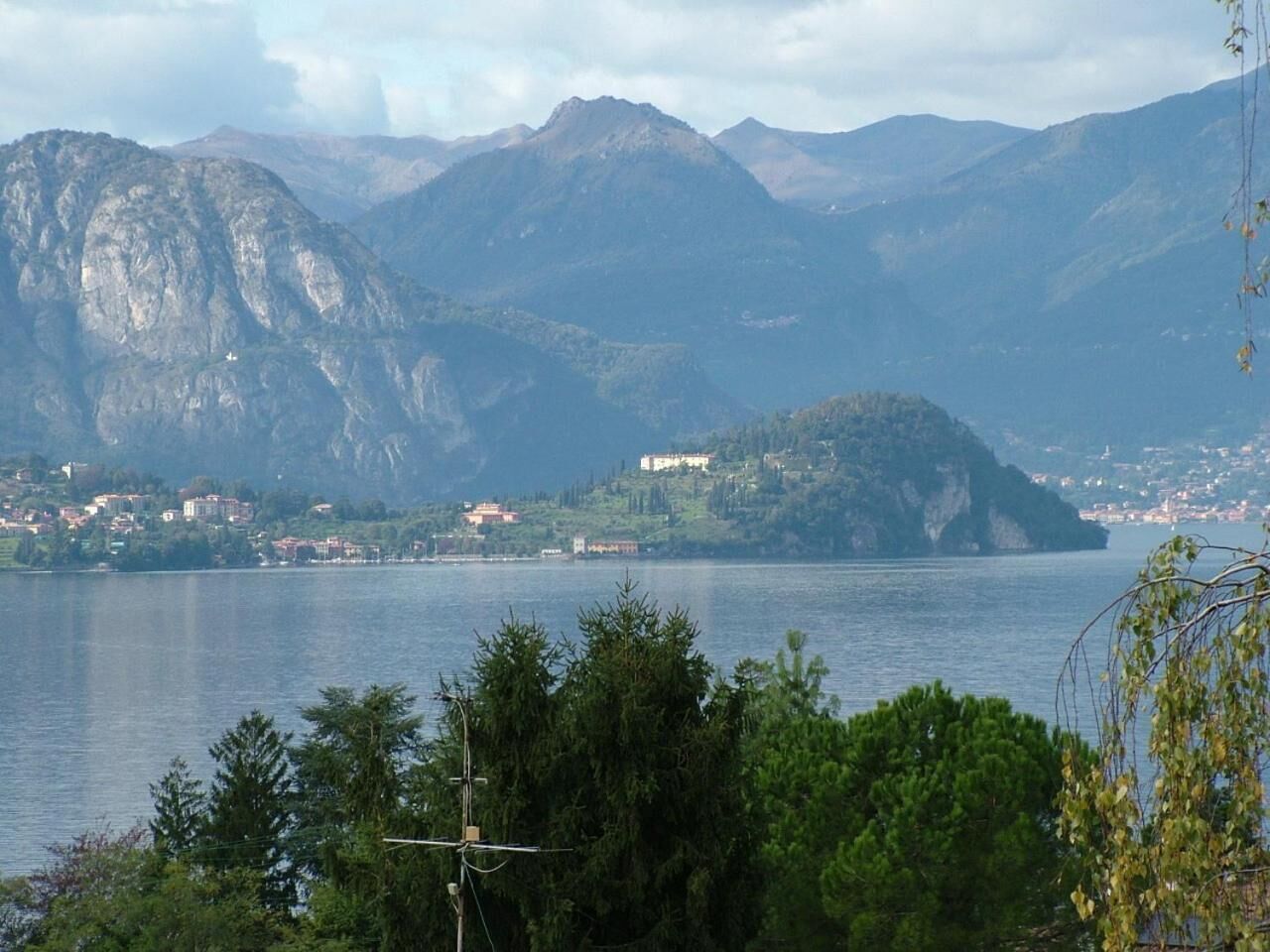 A mountainous landscape with a lake, buildings on the hills, and dense greenery in the foreground.