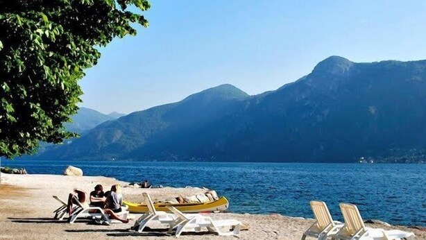 Une plage avec des chaises longues et un bateau jaune, avec des montagnes en arrière-plan.