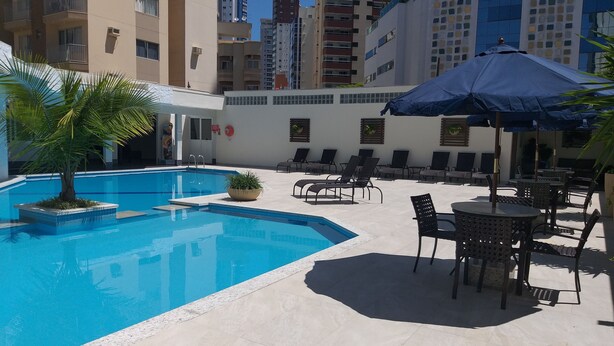 A swimming pool with lounge chairs and umbrellas, surrounded by high-rise buildings.