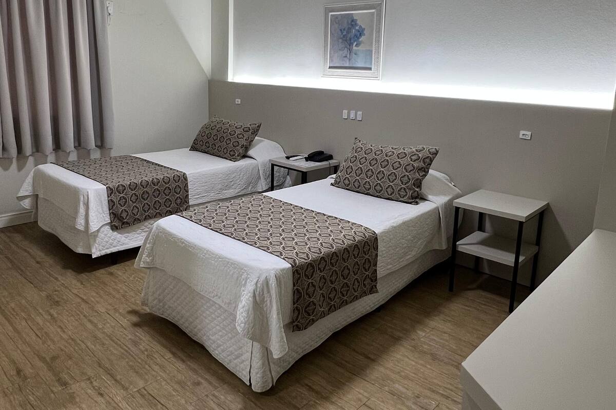 A hotel room with two beds, a bedside table, a small desk, and a framed picture on the wall.