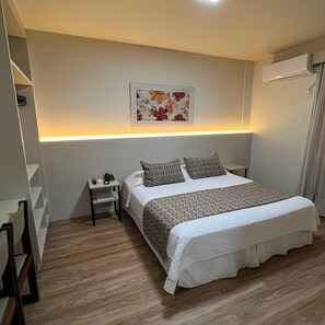 Una habitación de hotel con cama, mesita de noche y aire acondicionado instalado en la pared.