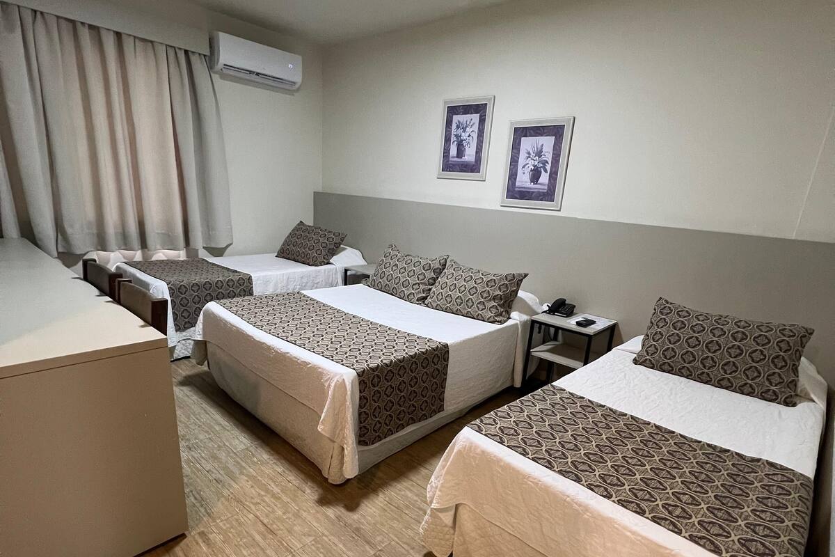 A hotel room with three beds, a desk, and an air conditioning unit.