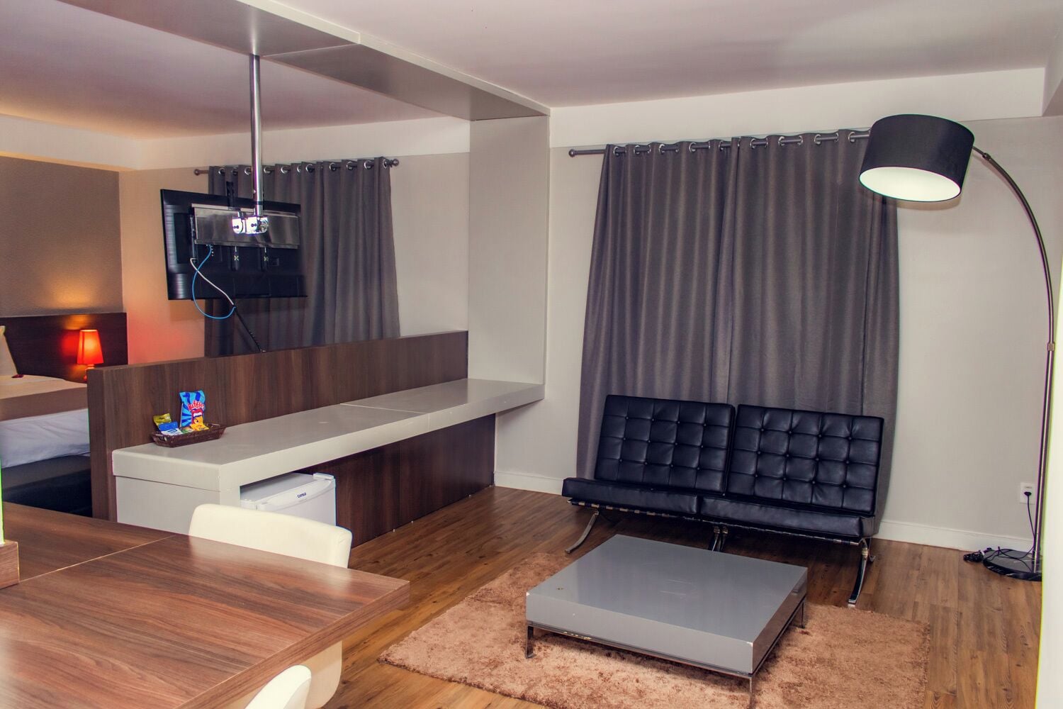 Una camera d'albergo moderna con una scrivania in legno, un divano nero, una TV a schermo piatto montata a parete e un'ampia finestra con tende.
