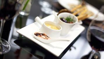 Une table à manger avec une assiette blanche contenant un dessert, deux tasses blanches avec des sauces et un verre de vin rouge.