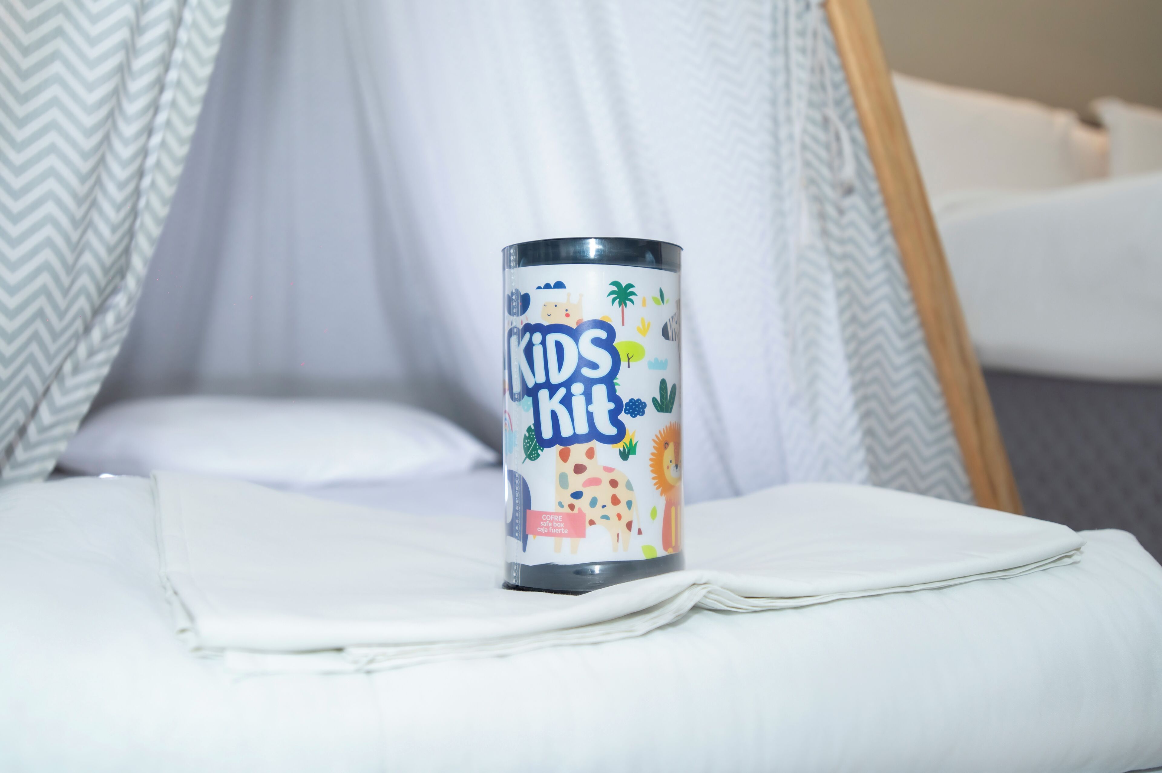A bed with a white sheet and a metal container labeled "Kids Kit" on it.