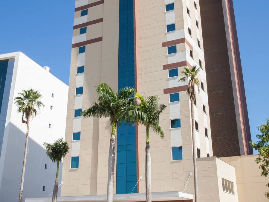 Un hotel alto con una fascia verticale blu al centro, diversi piani e palme sullo sfondo.