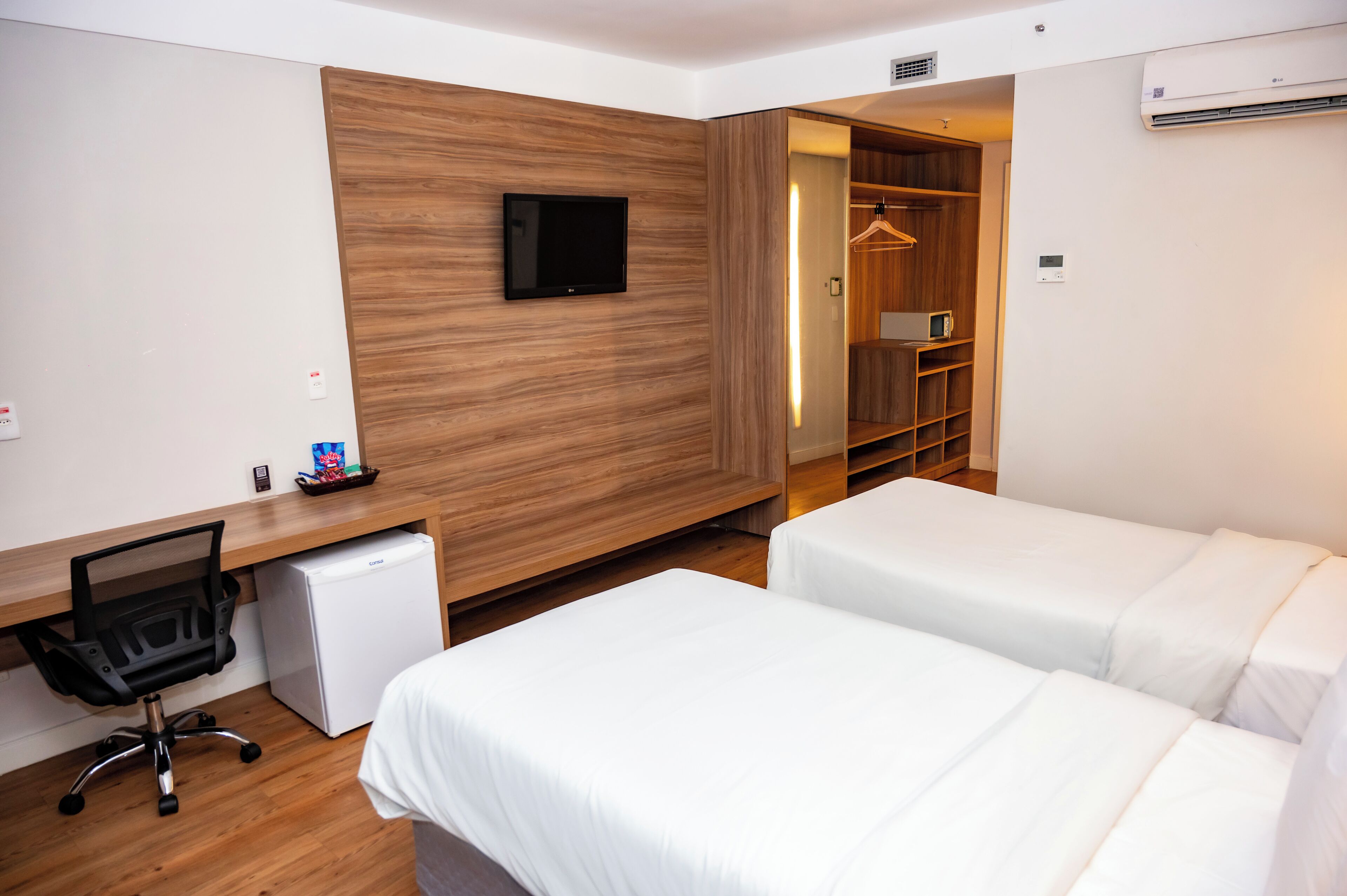 Habitació d'hotel amb paret d'accent de fusta, televisió de pantalla plana, escriptori amb ordinador, nevera petita i dos llits.
