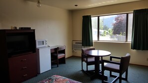 A small, furnished room with a television, microwave, and refrigerator, a small table with chairs, and a window with curtains. - Safari Inn (Winston)