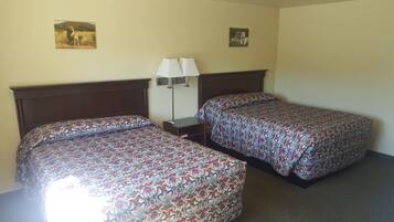 Habitación de hotel con dos camas, una mesita de noche, una lámpara y dos cuadros en la pared.