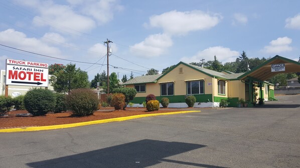 A motel with a green and beige exterior, a clear sign indicating truck parking, and a small office with a green roof.