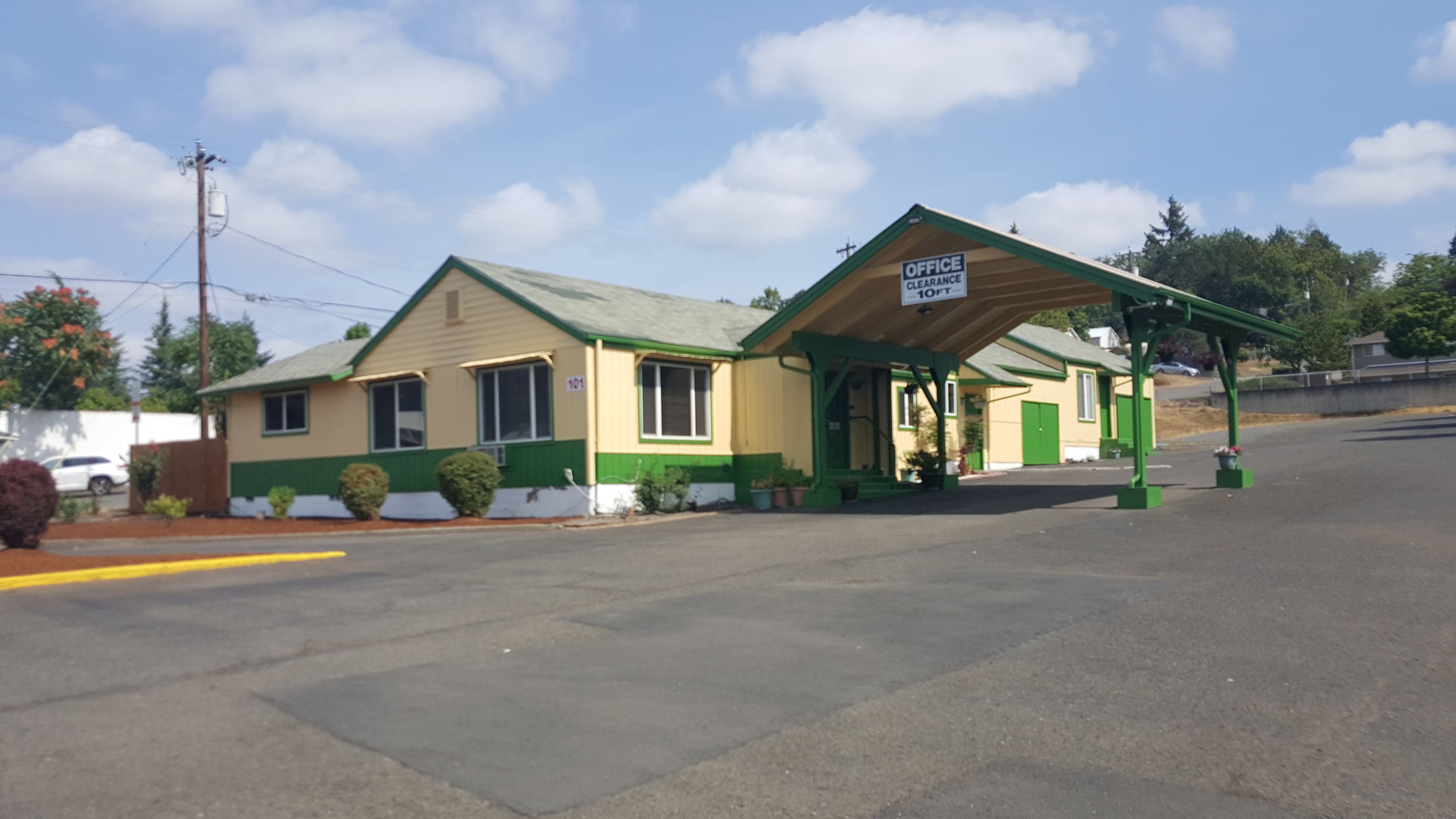 A small, single-story building with a green and beige exterior, a covered entrance, and a sign indicating an office and clearance.