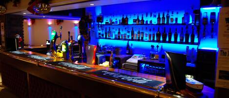 Una zona de bar con barra, estantes llenos de botellas y un letrero de neón.