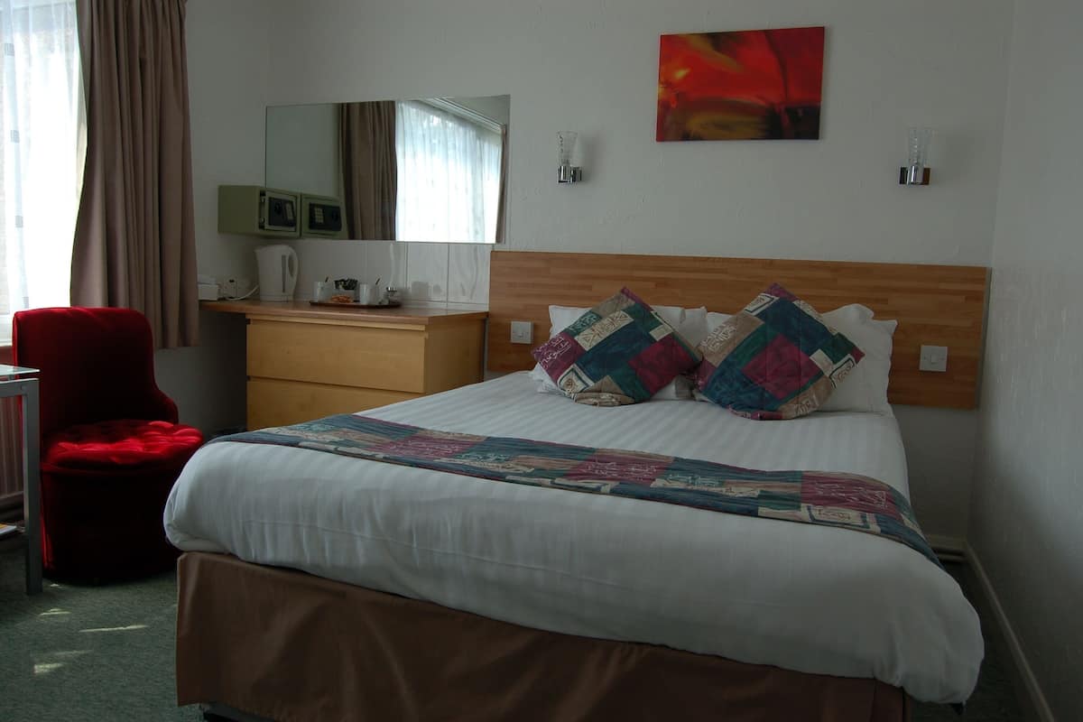 A hotel room with a bed, a desk, a chair, a mirror, and a painting on the wall.