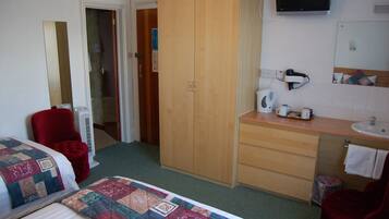 Hotelkamer met een bed, een rode stoel, een houten garderobe, een badkamer met een wastafel en spiegel, en een televisie aan de muur.