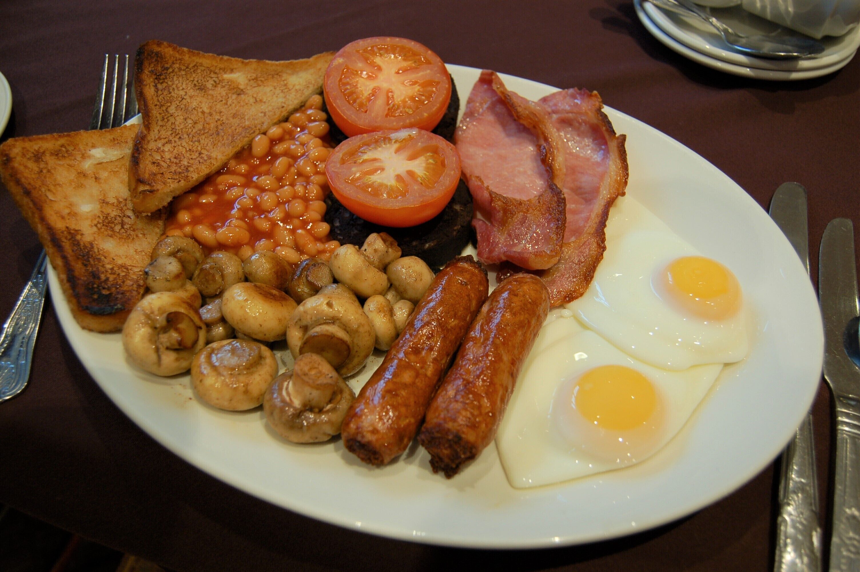 Une assiette de nourriture pour le petit-déjeuner comprenant des toasts, des œufs, du bacon, des tomates, des haricots, des champignons et des saucisses.