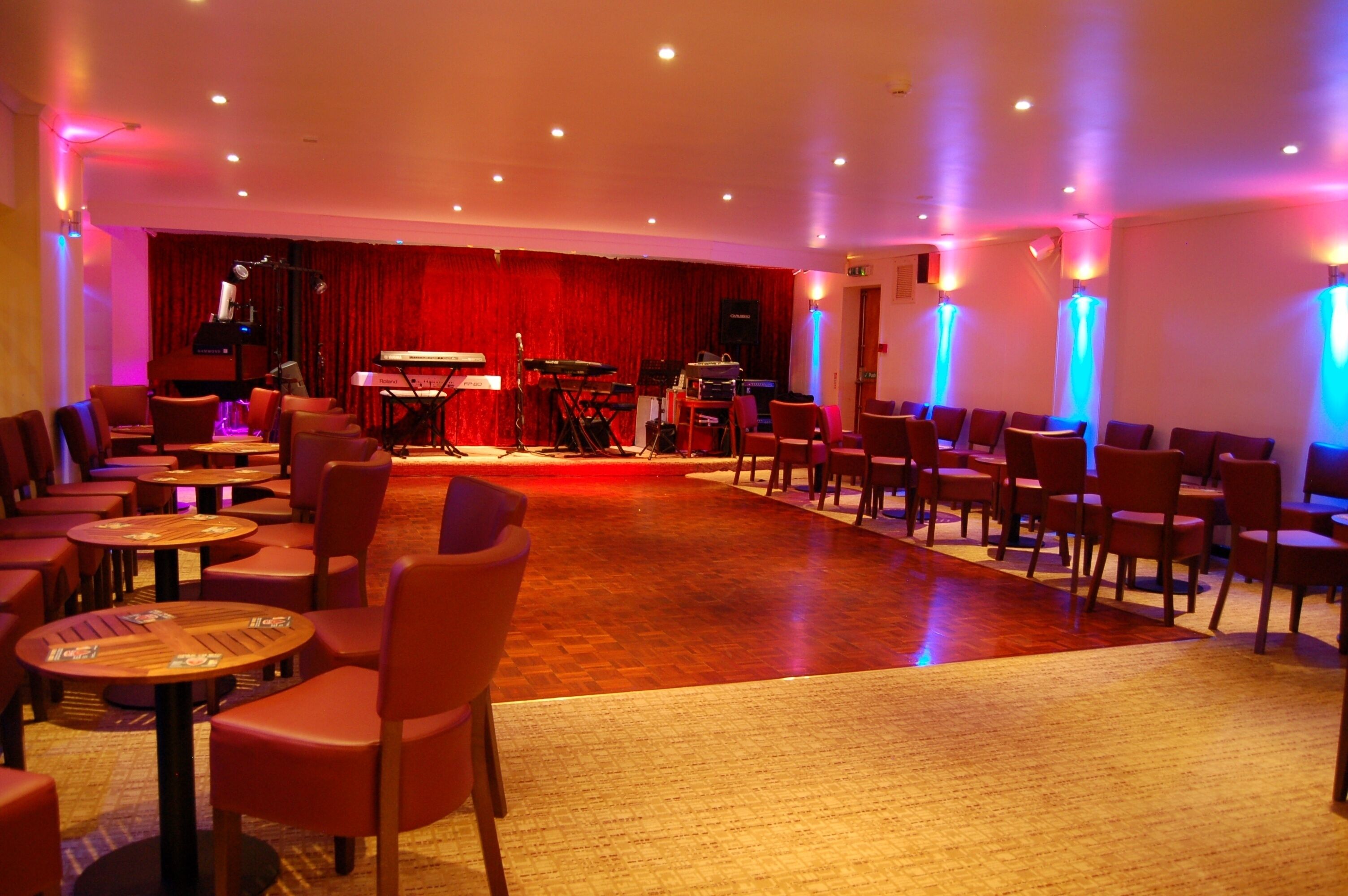 Una habitación amplia con un escenario, varias mesas y sillas dispuestas para un evento.