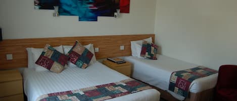 A hotel room with two beds, a wooden headboard, a red chair, and abstract wall art.