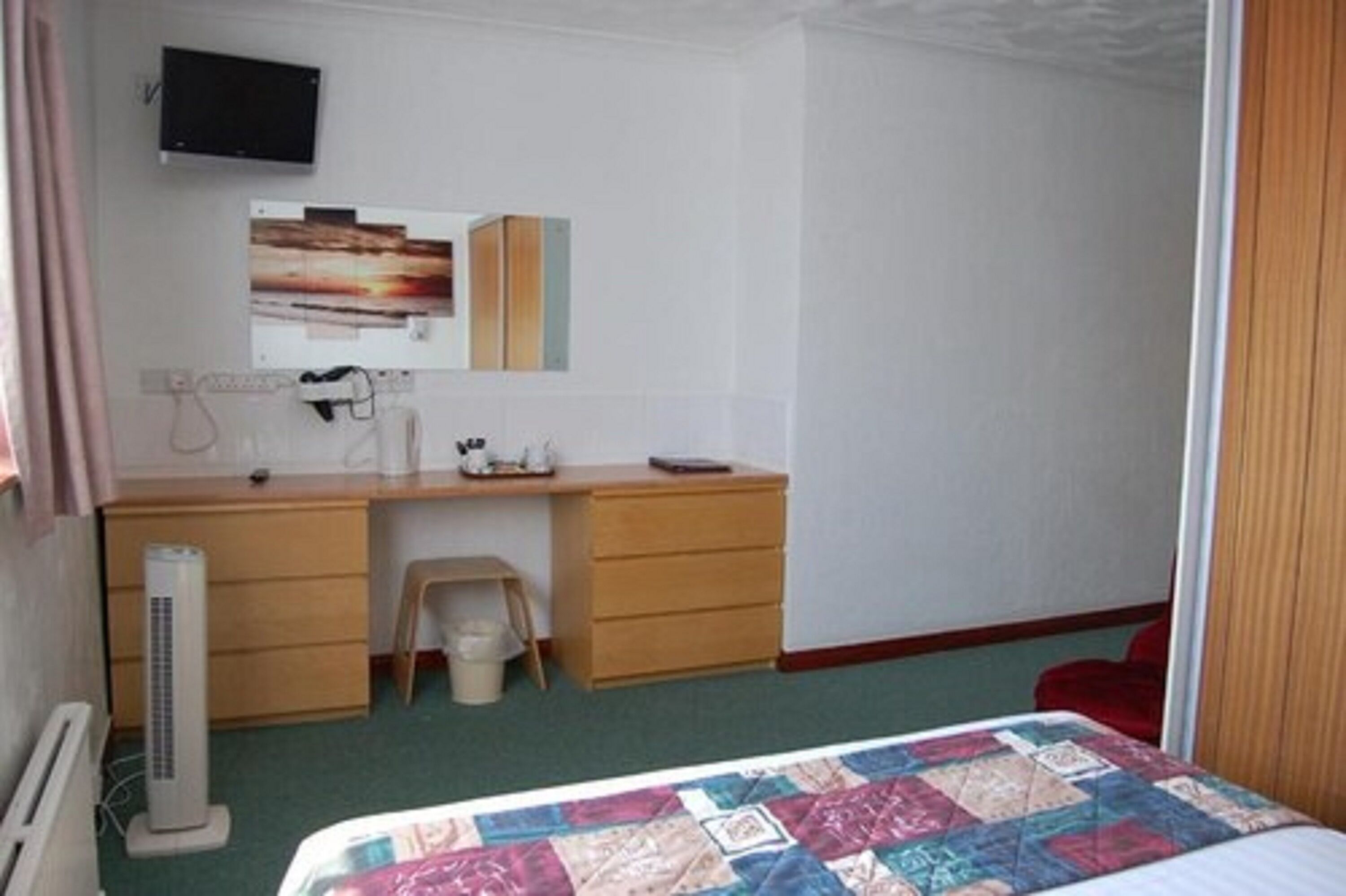 A bedroom with a bed, a desk, a chair, a television, and a small stool.