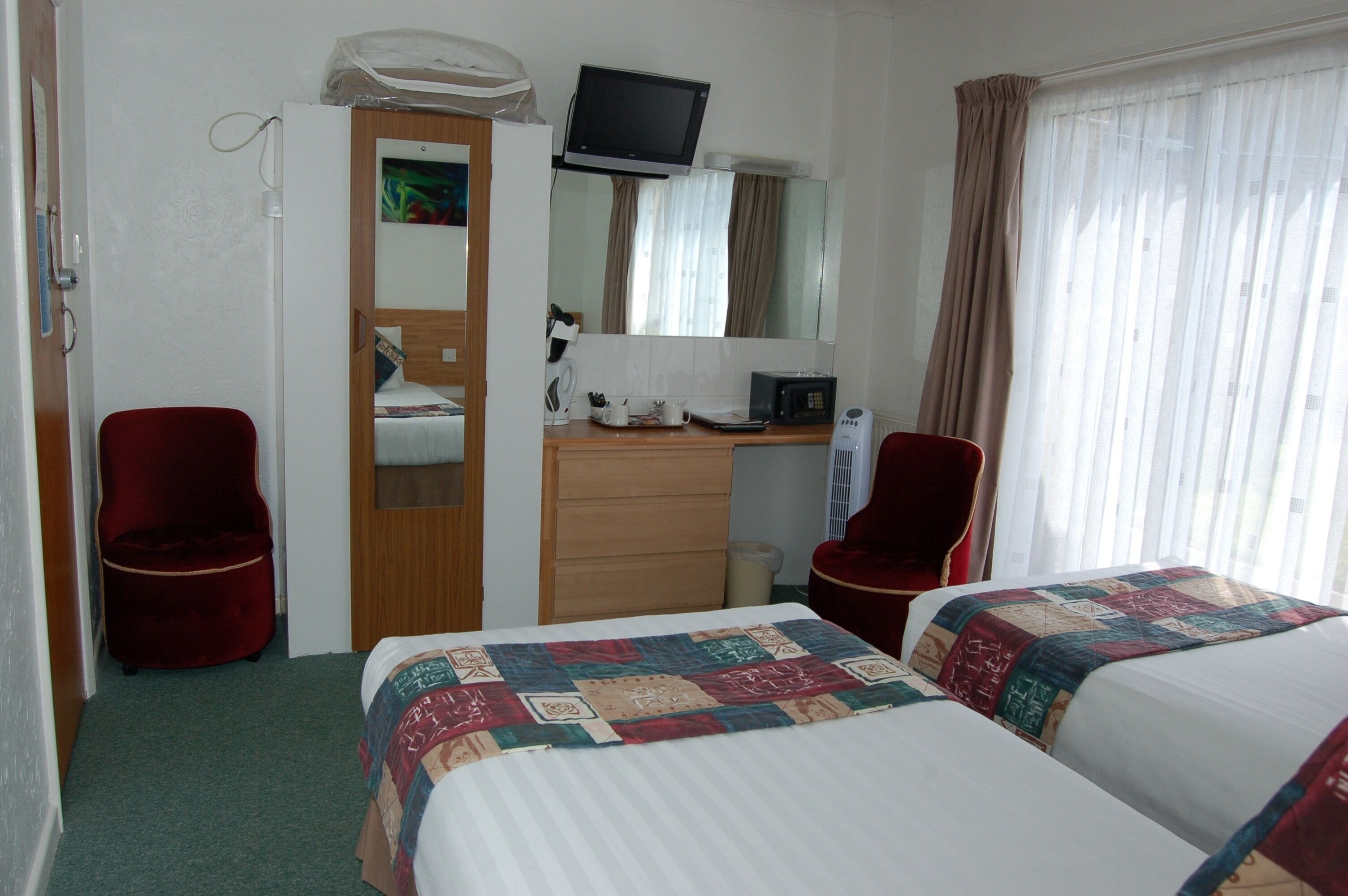 A hotel room with two beds, a desk with a computer, a TV, and a mirror.