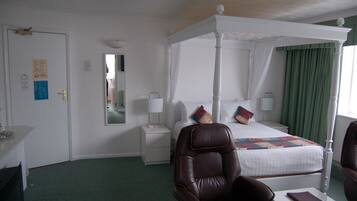 A four-poster bed with a canopy, a nightstand, a mirror, and a chair in a hotel room.