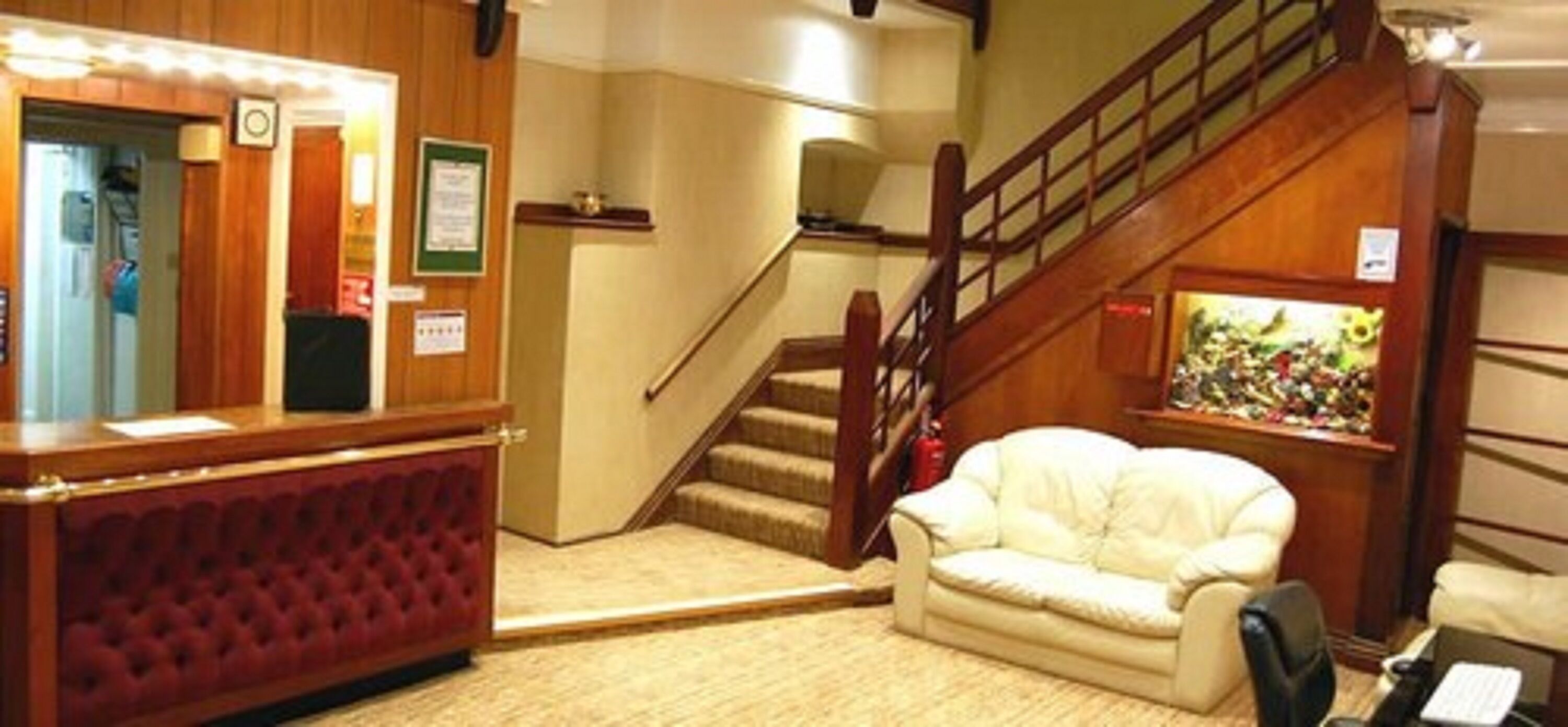 Un hall d’entrée avec un comptoir de réception, un escalier, un canapé blanc et un petit aquarium.