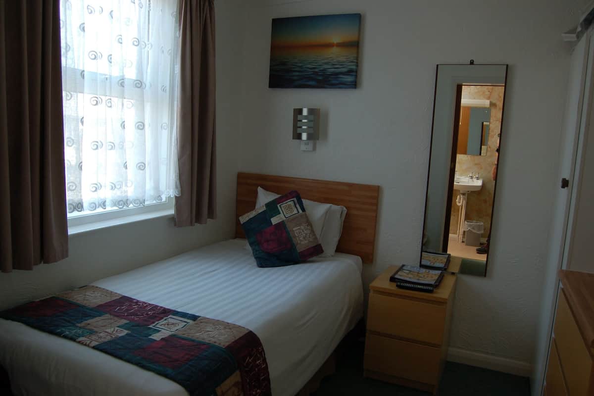 A hotel room with a bed, a bedside table, a mirror, and a window with curtains.