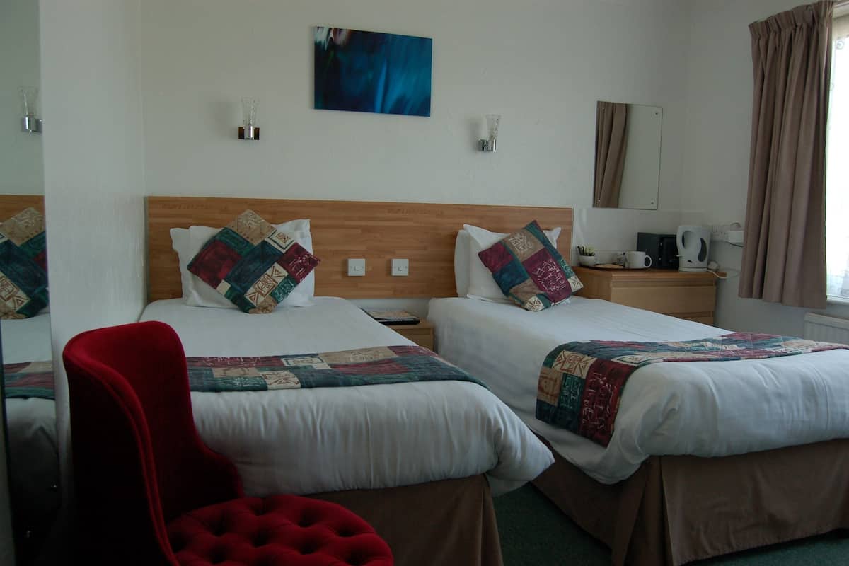 A hotel room with two beds, a red chair, a coffee maker, and a painting on the wall.